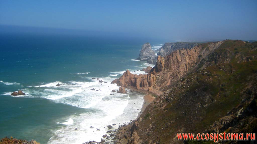 Escarpment cliffs on the Atlantic Ocean and sandy beach in the surf at Cape Roco (Cabo da Roca) - the western most point of Eurasia mainland. National Park of Sintra-Cascais on the west coast of Portugal